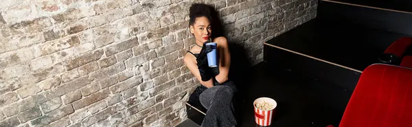 Привлекательная африканская американка в вечернем наряде сидит с напитком и смотрит в камеру, баннер — стоковое фото