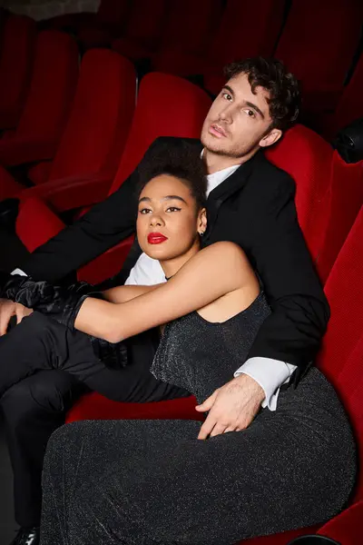 Attraktives multikulturelles Paar in schwarzen eleganten Kleidern posiert am Valentinstag liebevoll im Kino — Stockfoto