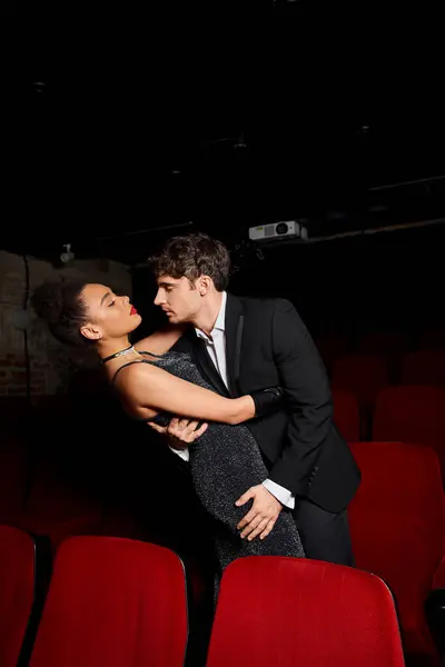 Attrayant couple multiethnique en tenue de soirée noire posant dans la danse au cinéma le jour de la Saint-Valentin — Photo de stock