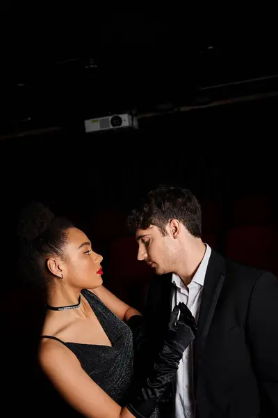Sensual young multicultural couple in black attires looking at each other at cinema on date — Stock Photo