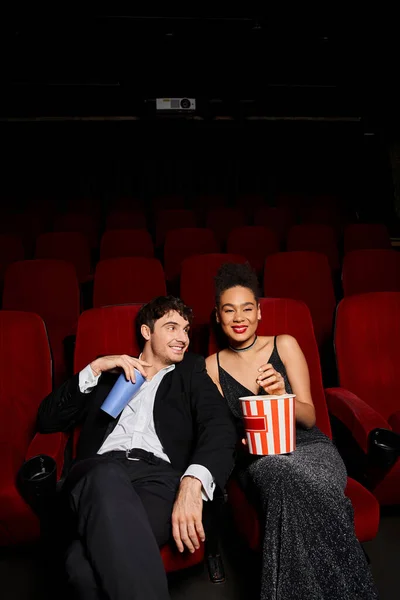Fröhliches multiethnisches Paar in schwarzer schicker Kleidung mit Limo und Popcorn und glücklich lächelnd — Stockfoto