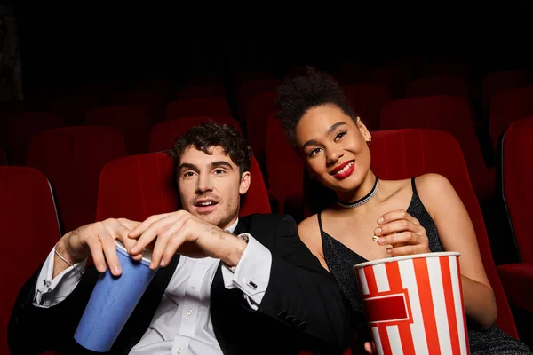 Cheerful multicultural couple enjoying movie at cinema and holding soda and popcorn, Valentines day — Stock Photo
