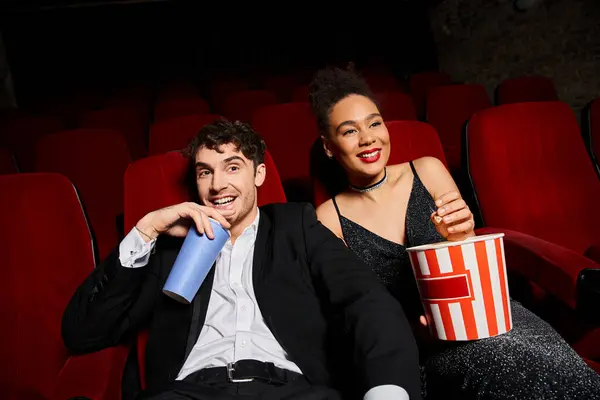 Alegre casal multiétnico em trajes elegantes desfrutando de filme no cinema enquanto na data, dia dos namorados — Stock Photo