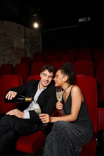 Cheerful multicultural couple in evening chic attires drinking champagne at cinema on Valentines day — Stock Photo