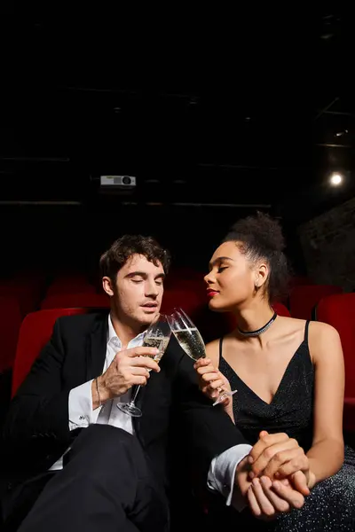 Attraktives junges, vielseitiges Paar in Abendkleidung, das am Valentinstag im Kino Gläser klimpert — Stockfoto