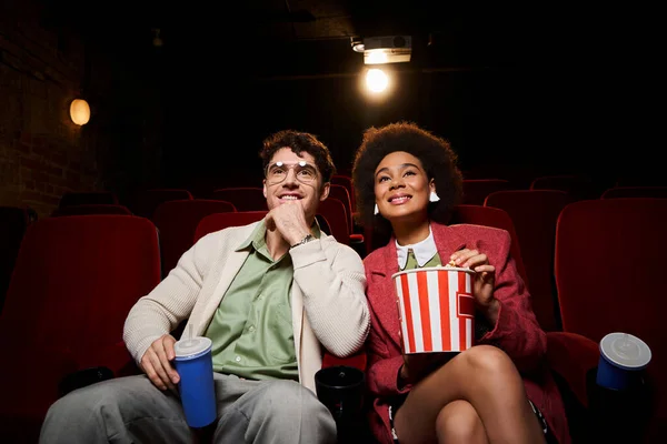 Jovem alegre diverso casal em vibrante roupa casual sentado em cadeiras de cinema vermelho, dia dos namorados — Fotografia de Stock