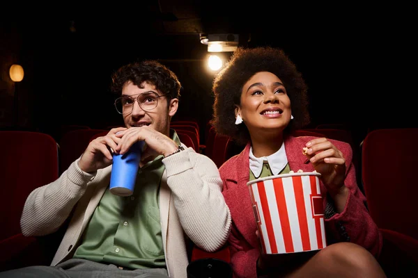 Cheerful beautiful multicultural couple in retro casual outfits enjoying movie on their date — Stock Photo