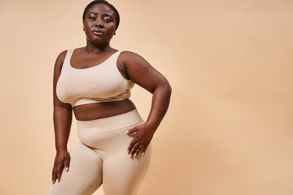 Plus size afrikanisch-amerikanische Frau in Unterwäsche schaut in die Kamera auf beigem Hintergrund, Körper positiv — Stockfoto