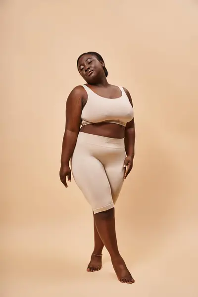 Gracieux modèle afro-américain taille plus en tenue beige posant sur un fond assorti — Photo de stock