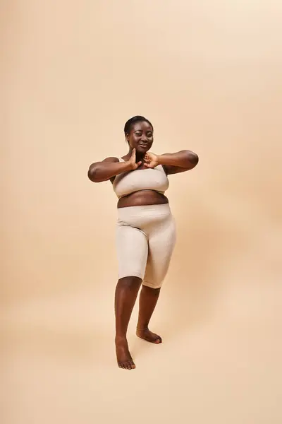 Souriant modèle afro-américain taille plus en tenue beige posant sur un fond assorti — Photo de stock