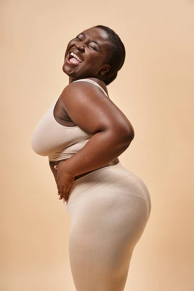 Cheerful plus size african american woman posing against matching backdrop, body positive — Stock Photo