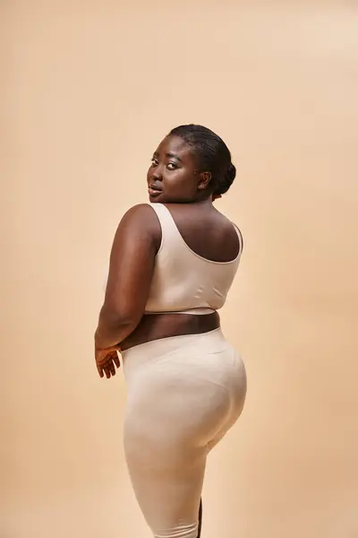 Jeune femme afro-américaine taille plus en sous-vêtements beige posant sur fond assorti — Photo de stock