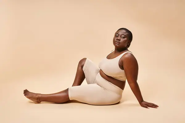Plus size african american young woman in beige underwear posing against matching backdrop — Stock Photo