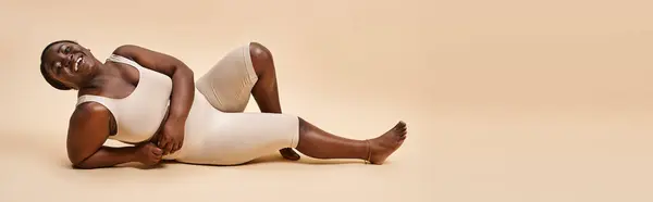 Bannière de heureuse plus la taille afro-américaine jeune femme inclinant sur fond beige — Photo de stock