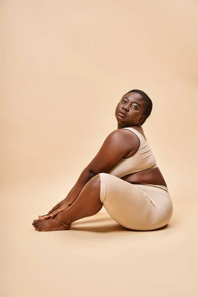 Body positive, african american young woman in beige underwear posing against matching backdrop — Stock Photo
