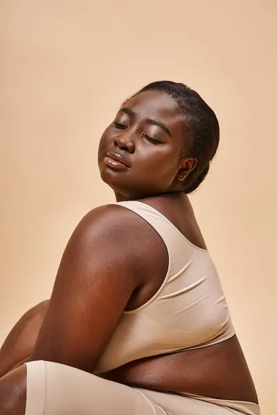 Body positive, plus size african american woman in beige underwear posing against matching backdrop — Stock Photo