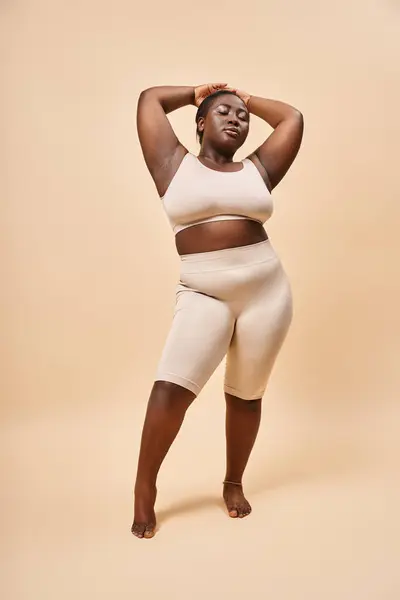 Plus size afrikanisch-amerikanisches Model in Unterwäsche stehend mit erhobenen Händen vor beigem Hintergrund — Stockfoto