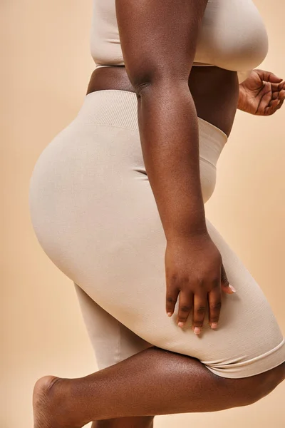 Vue recadrée de plus taille femme afro-américaine en sous-vêtements posant sur fond beige, corps courbé — Photo de stock
