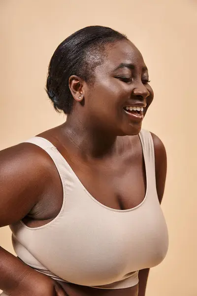 Glückliche afrikanisch-amerikanische Plus-Size-Frau in beiger Unterwäsche, die Selbstliebe und Selbstvertrauen umarmt — Stockfoto