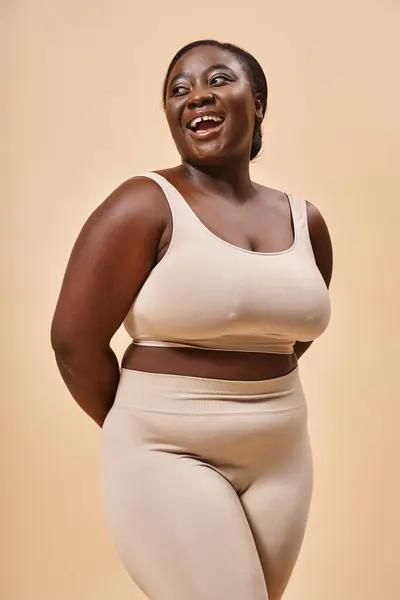 Щаслива жінка плюс розмір жінка в бежевій білизні сміється в студії, тіло позитивне і самоповажне — стокове фото