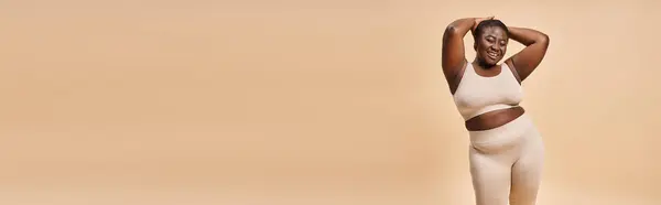 Heureux plus taille femme en sous-vêtements beige posant avec les mains près de la tête, corps bannière positive — Photo de stock