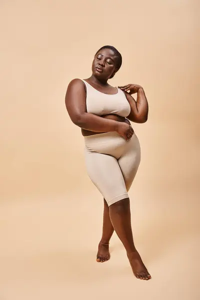 Плюс розмір жінки в нижній білизні позує на бежевому тлі, концепція позитивного тіла і самоповаги — стокове фото