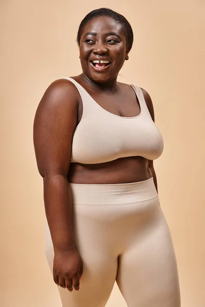 Alegre mulher plus size em roupa interior bege rindo e olhando para longe, corpo positivo e auto-estima — Fotografia de Stock