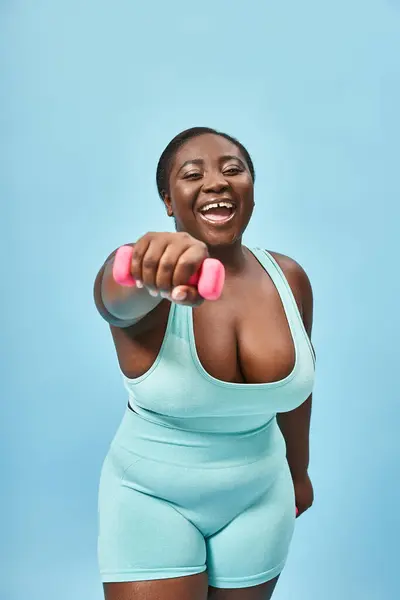 Alegre más tamaño mujer en azul activo desgaste ejercicio con mancuerna a juego fondo - foto de stock
