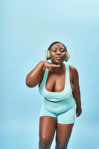 Plus size donna afroamericana in abbigliamento sportivo ascoltare musica in cuffia e labbra indolenzite — Foto stock