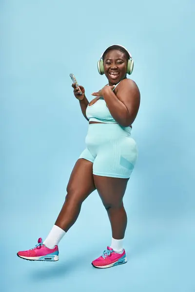 Mujer afroamericana de tamaño grande escuchando música en auriculares conectados a teléfonos inteligentes - foto de stock
