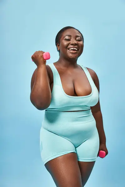 Corpo positivo, plus size woman in blue active wear exercitando-se com halteres no fundo correspondente — Fotografia de Stock