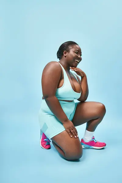Volle Länge glücklich plus Größe Sportlerin in Radlerhosen sitzt auf blauem Hintergrund, Körper positiv — Stockfoto