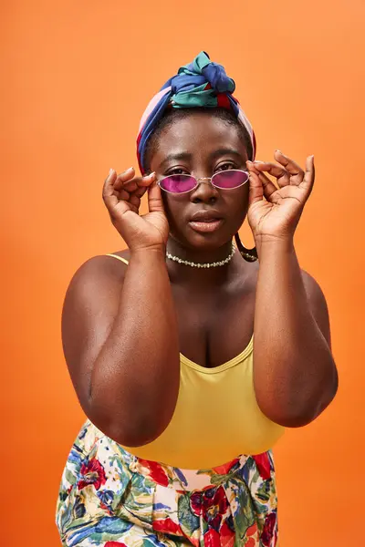 Femme afro-américaine à la mode plus la taille en foulard portant des lunettes de soleil tendance sur orange — Photo de stock
