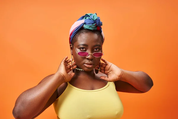 Élégant plus la taille femme afro-américaine en foulard et lunettes de soleil à la mode sur fond orange — Photo de stock