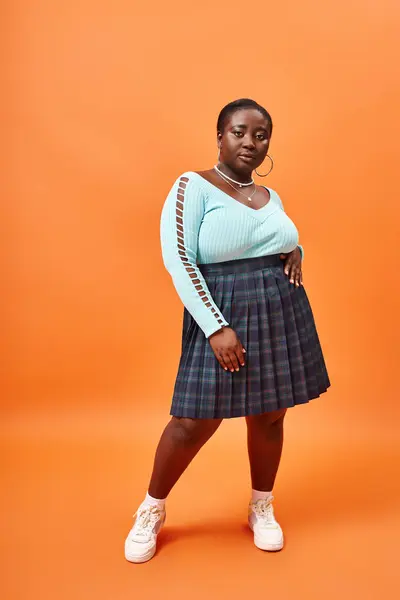 Fashion-forward plus taille femme afro-américaine en jupe à carreaux et bleu manches longues sur orange — Photo de stock