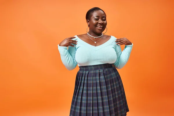 Heureux plus la taille femme afro-américaine en jupe à carreaux et bleu manches longues sur fond orange — Photo de stock