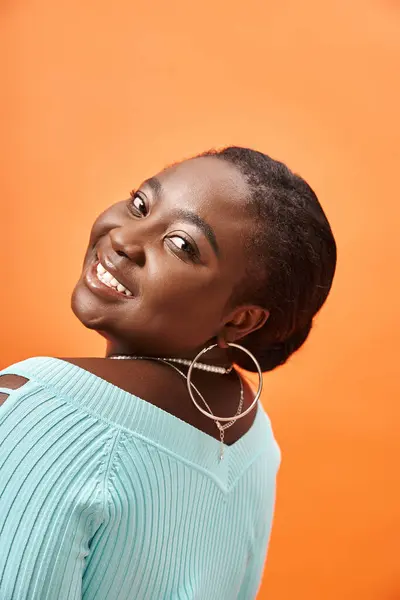 Portrait of charming plus size african american woman in blue long sleeve smiling on orange — Stock Photo