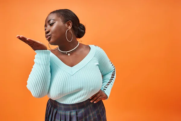Playful plus size african american woman in plaid skirt and long sleeve sending an air kiss — Stock Photo
