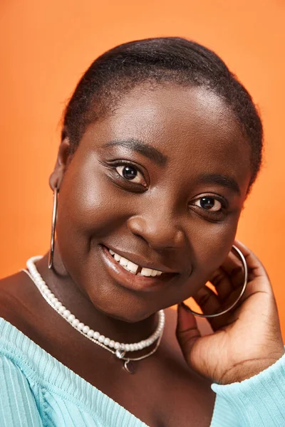 Portrait of joyful plus size african american woman in blue long sleeve smiling on orange — Stock Photo