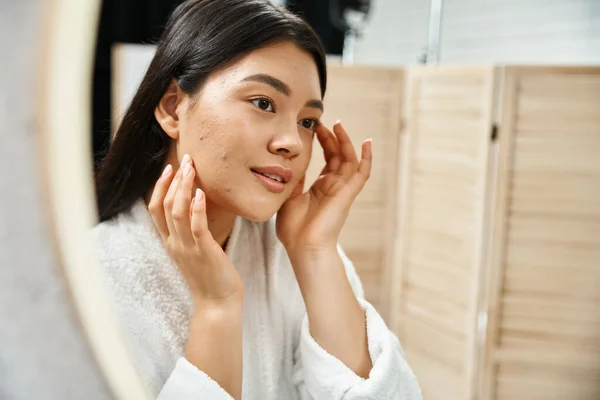 Junge asiatische Frau mit brünetten Haaren untersucht ihre Haut im Badezimmerspiegel, Hautzustand — Stockfoto