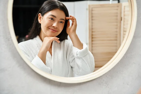 Cheerful asian girl with brunette hair examining her face with acne in bathroom mirror, skin issue — Stock Photo
