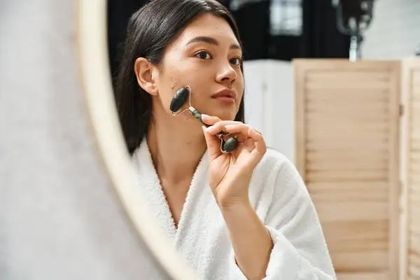 Young asian woman with brunette hair using jade roller for a facial massage in bathroom, skin care — Stock Photo