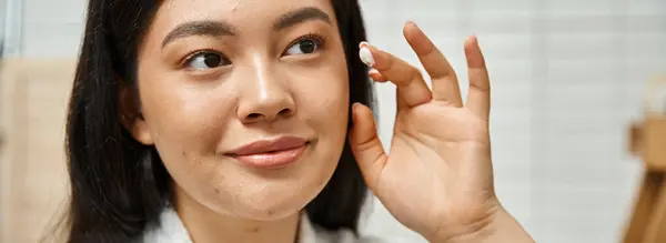 Bannière de jeune femme asiatique avec de l'acné appliquer de la crème sur le visage et regarder miroir dans la salle de bain — Photo de stock