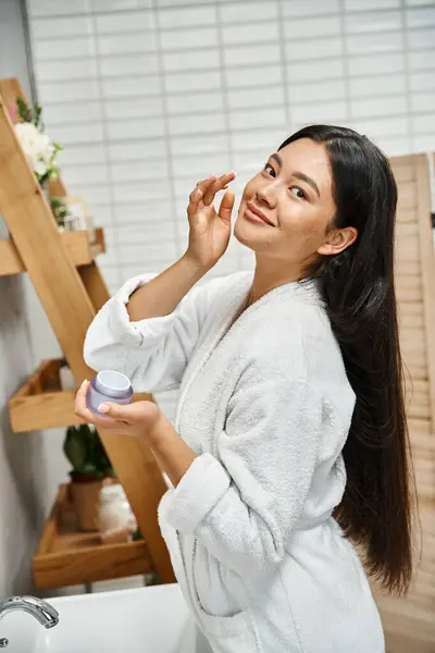 Happy and pretty asian woman with acne applying cream on face and smiling while looking at camera — Stock Photo