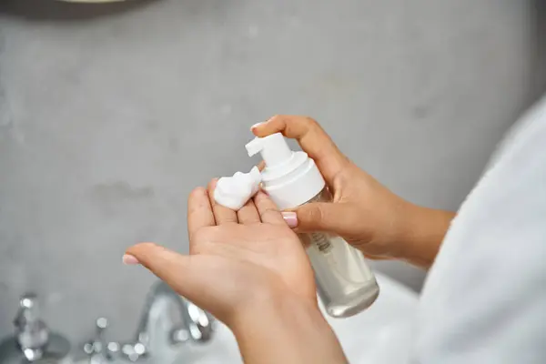 Vista recortada de la mujer joven en bata de baño preparándose para usar espuma de limpieza facial en el baño - foto de stock