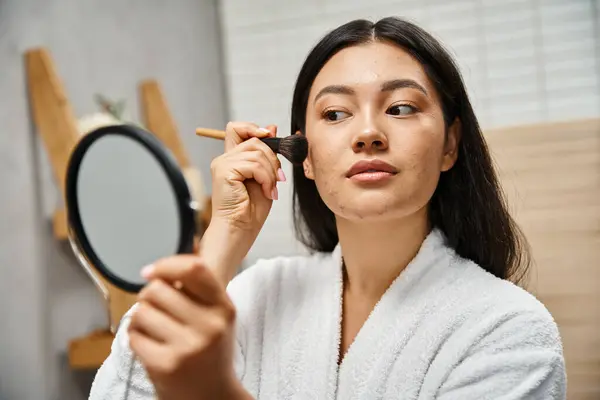 Jeune femme asiatique avec des cheveux bruns et l'acné application de poudre avec pinceau cosmétique, problèmes de peau — Photo de stock