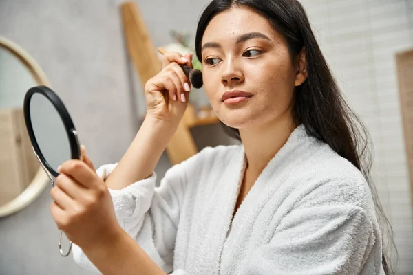 Красива азіатська жінка з брюнеткою наносить макіяж над шкірою, схильною до акне, косметичним пензлем — стокове фото