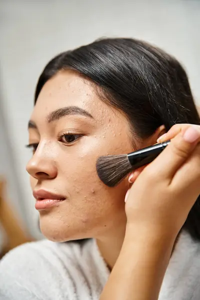 Bruna e giovane donna asiatica che applica polvere per il viso sulla pelle incline all'acne con pennello cosmetico — Foto stock