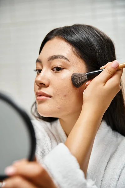 Brunette young asian woman applying face powder over acne-prone skin with cosmetic brush, makeup — Stock Photo
