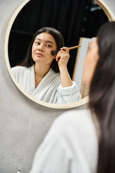 Молодая азиатка наносит порошок на кожу, склонную к прыщам, кистью на зеркало, макияж — стоковое фото